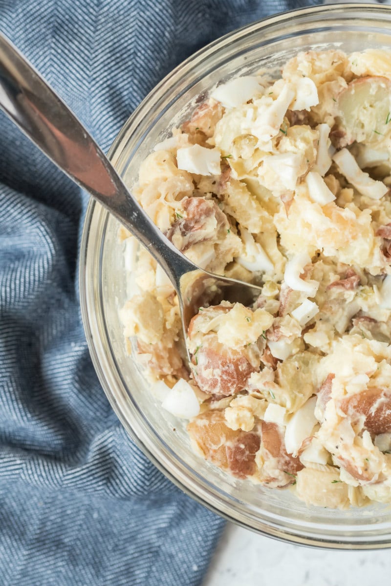 overhead shot of potato salad in a glass bowl with a serving spoon set on a blue napkin