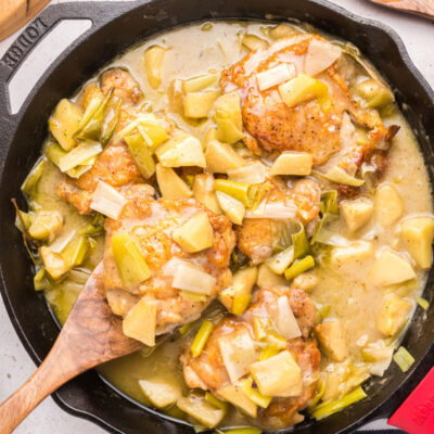 spooning chicken out of chicken, leek and apple stew in skillet