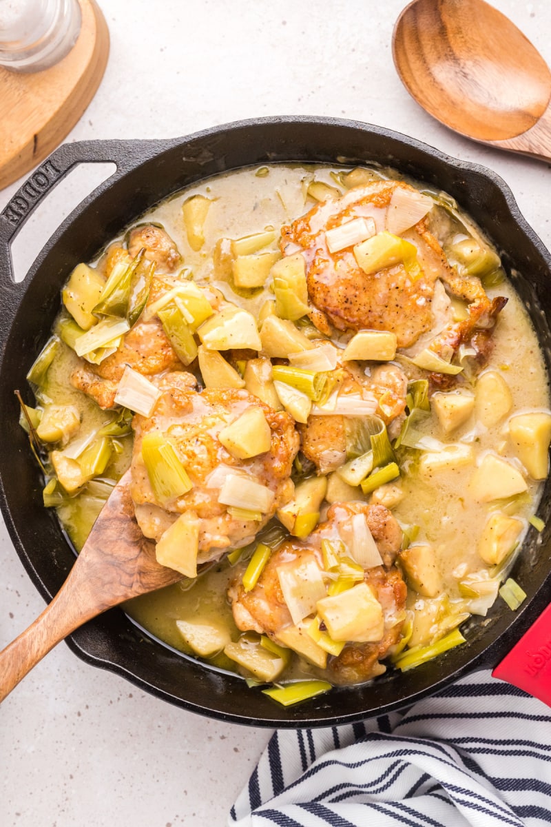 spooning chicken out of chicken, leek and apple stew in skillet