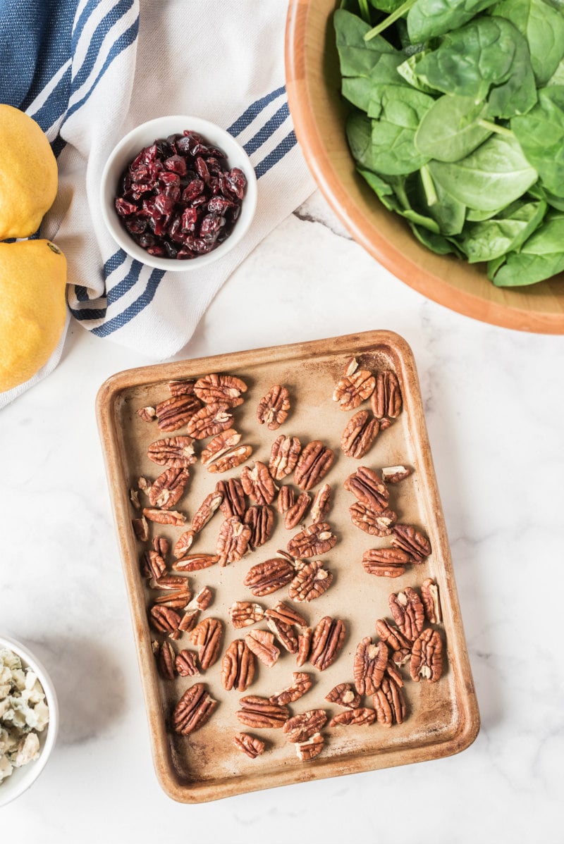 pecans on a baking sheet with ingredients for salad displayed