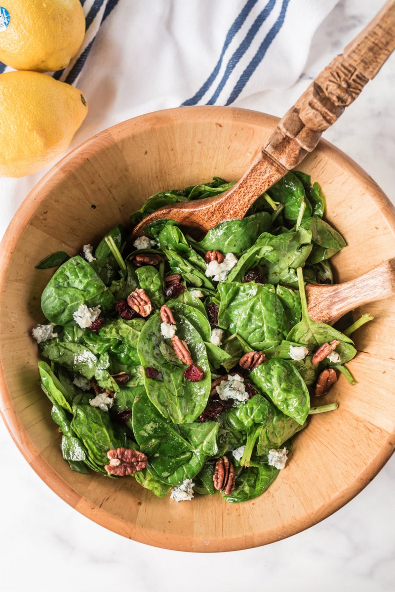 cranberry spinach salad in wooden bowl with salad servers