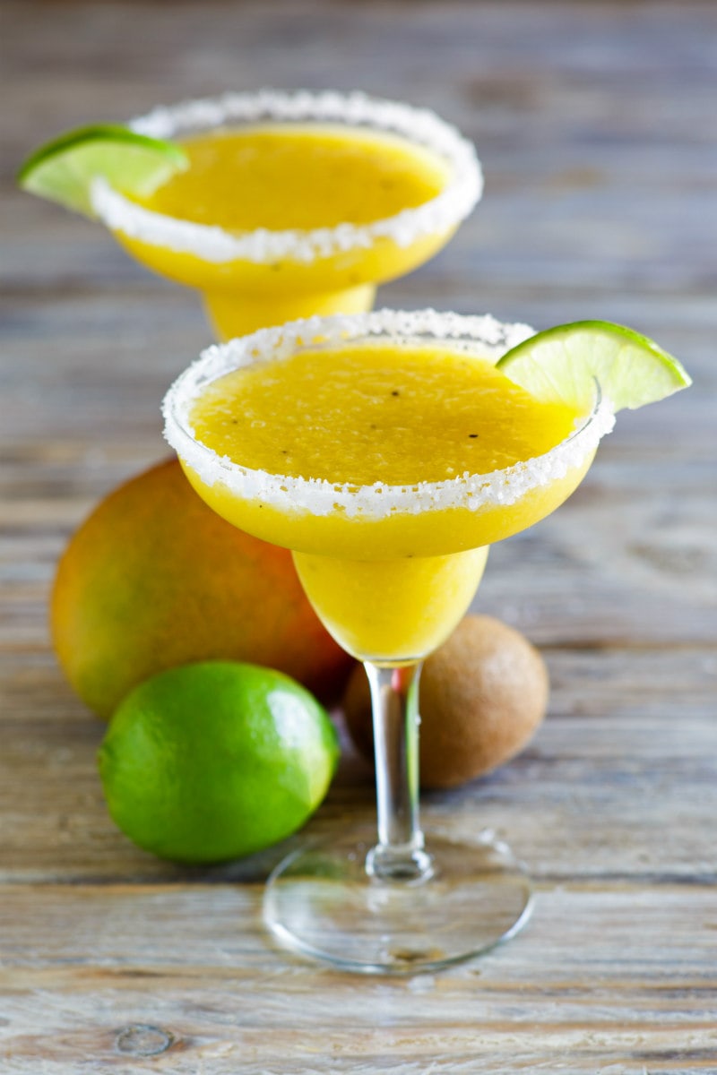 tropical margaritas in margarita glasses with lime wedge and fresh fruit displayed