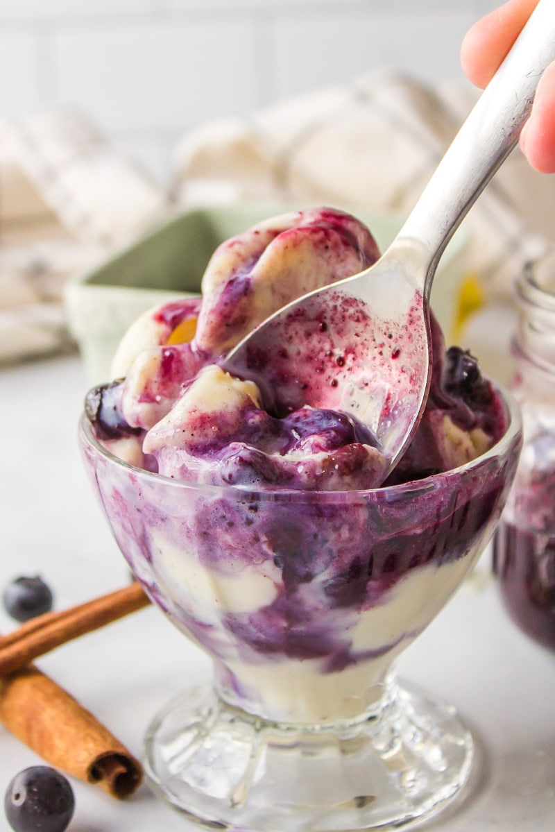 spoon inside dish of vanilla ice cream with hot blueberry sauce on top