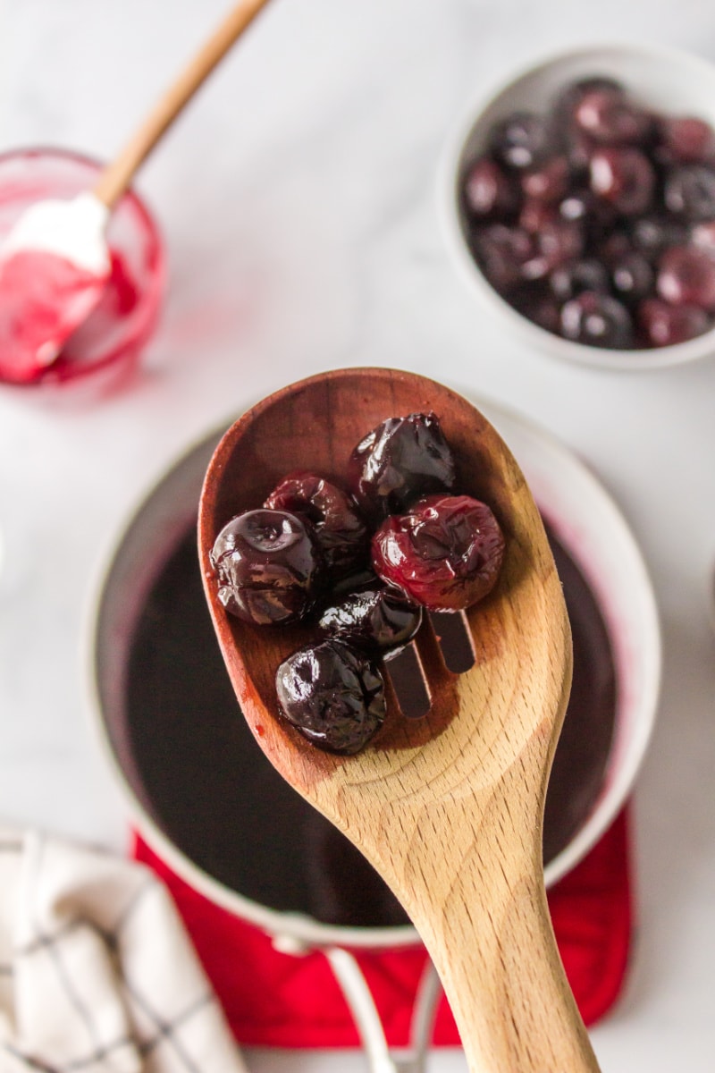 wooden spoon with hot cherry sauce on it over pan