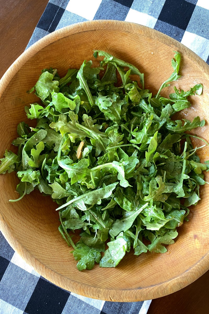 arugula tossed with dressing in wood bowl