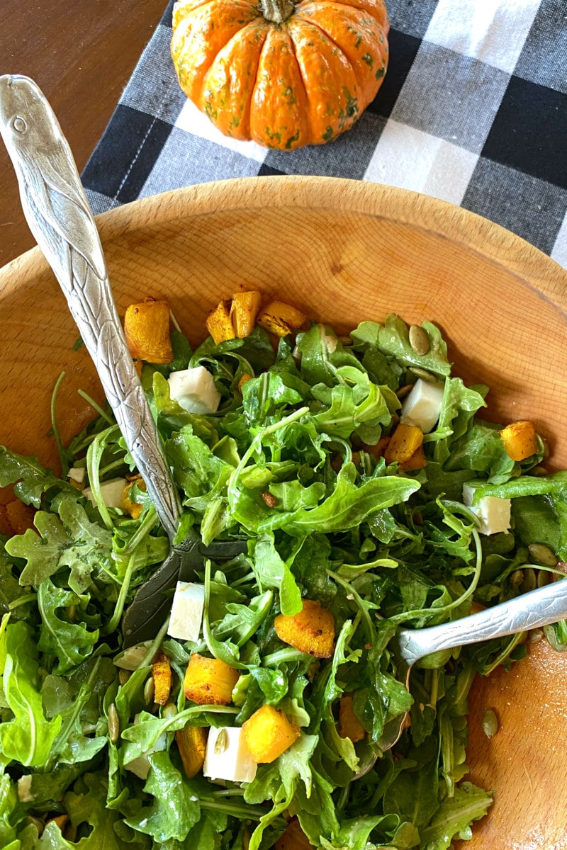 salad tongs tossing maple roasted pumpkin salad in wood bowl