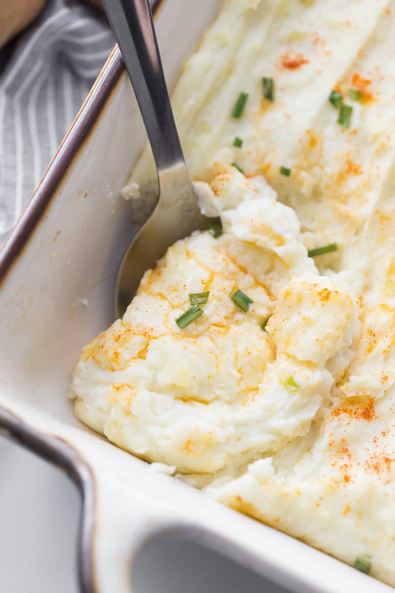 serving creamy oven baked mashed potatoes out of a white casserole dish