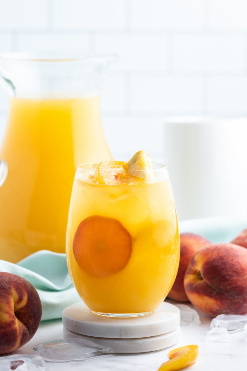 peach sangria in a glass with pitcher in background