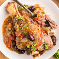 lamb shank on a plate topped with artichokes and olives