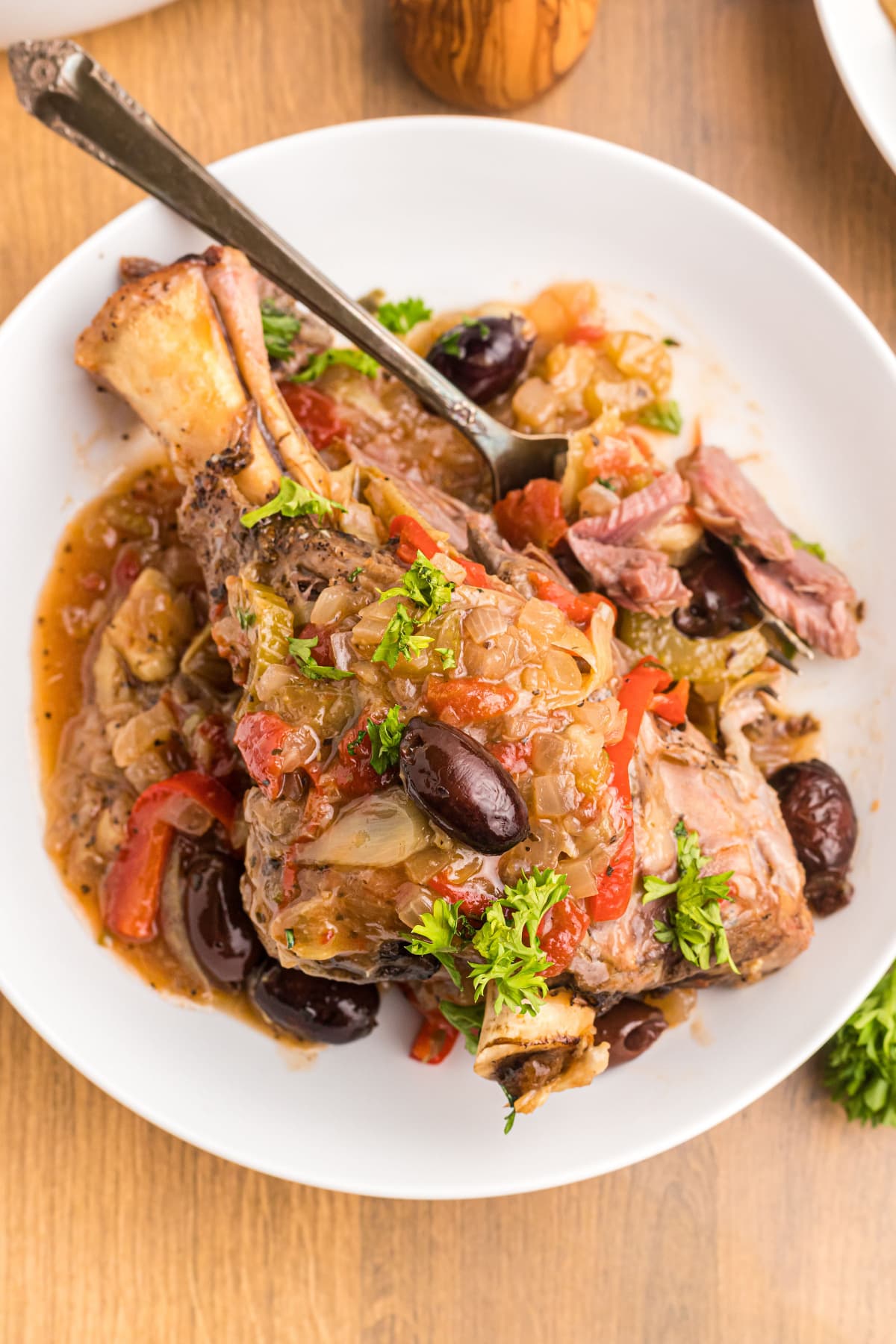 lamb shank on a plate topped with artichokes and olives