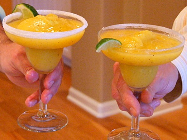 Two hands holding tropical margaritas in a cheers-like fashion