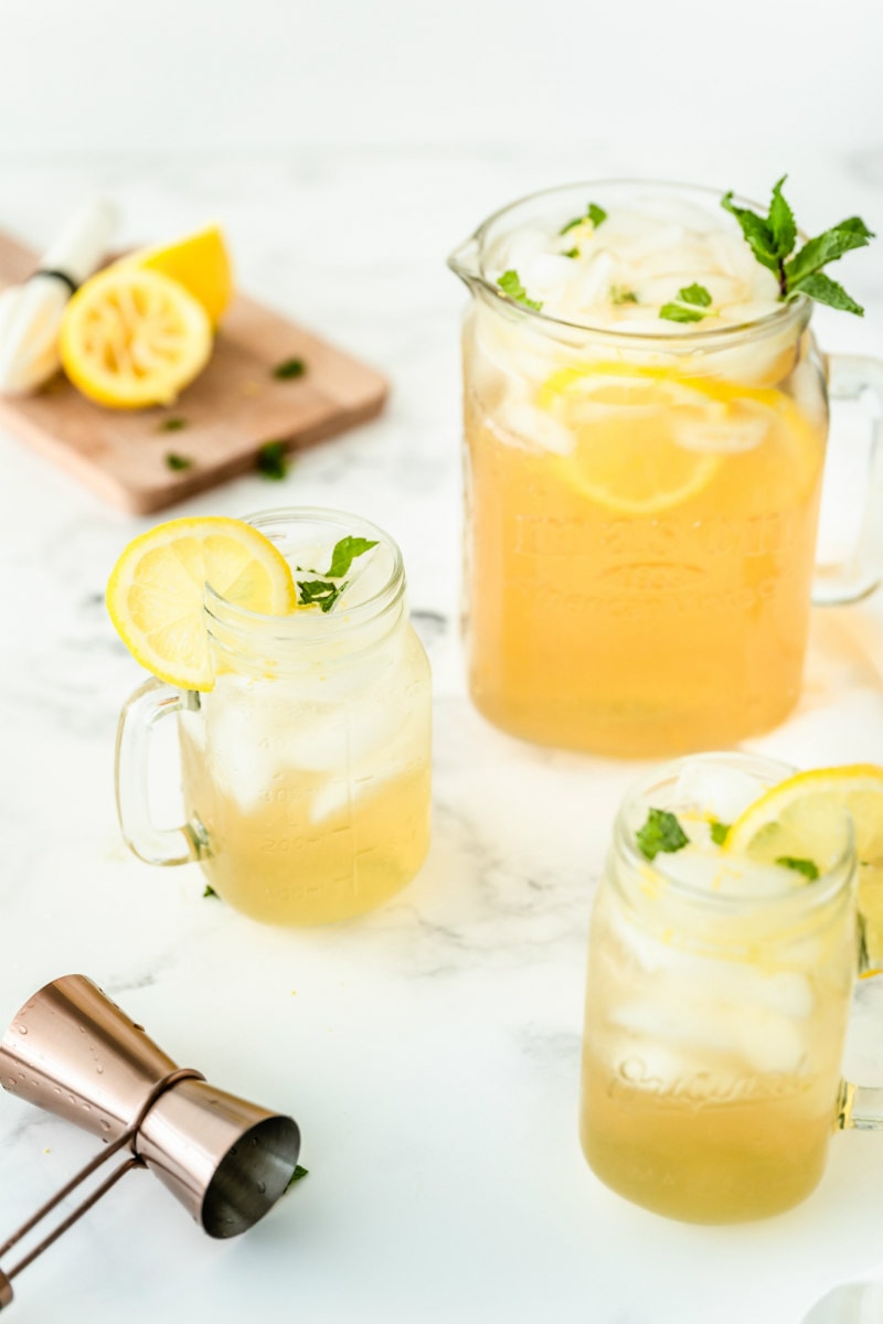 vodka lemonade in a pitcher with two servings in glass mugs. squeezed lemons in background