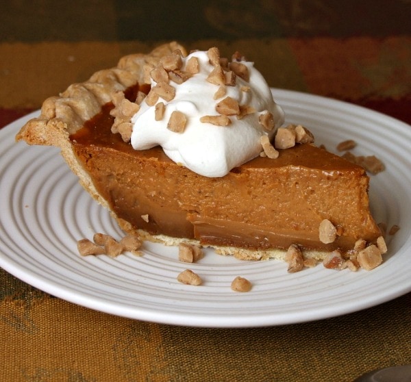 slice of pumpkin pie on a plate topped with whipped cream and toffee bits