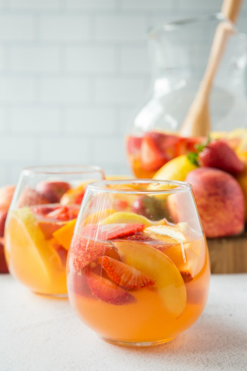 glasses of strawberry peach sangria with pitcher in background