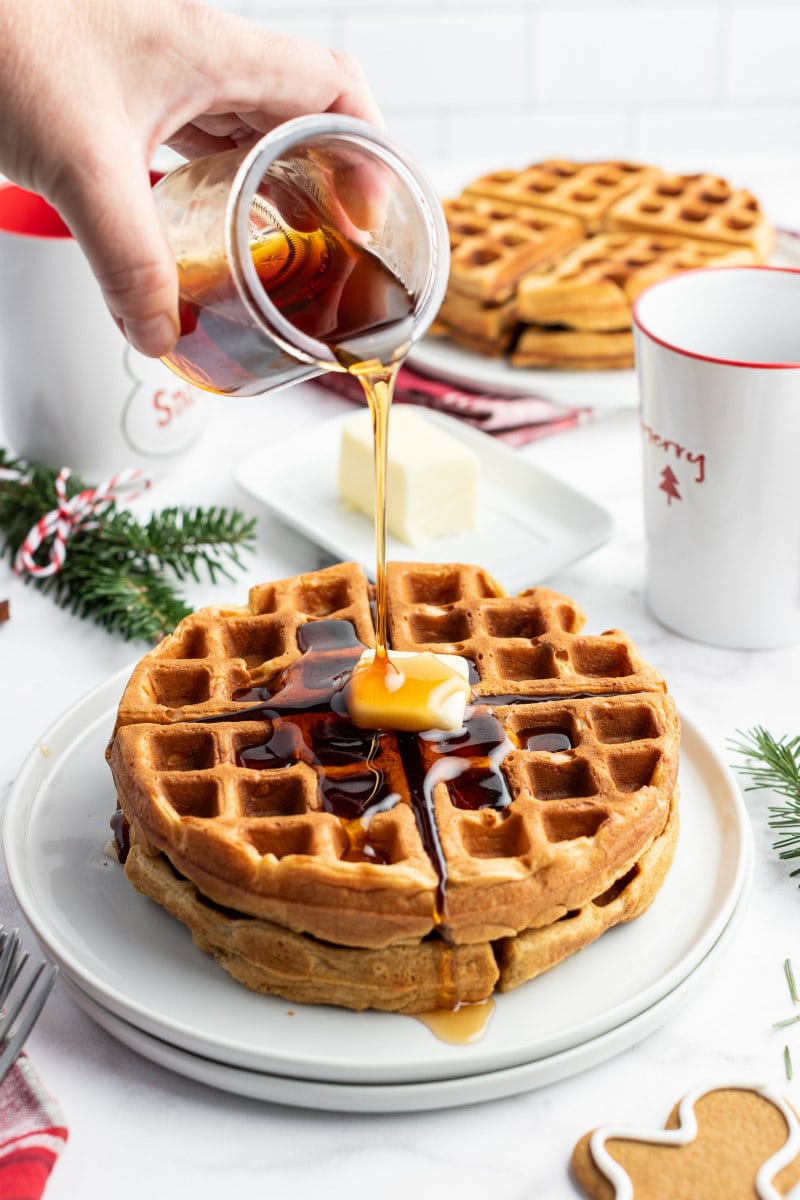 hand pouring syrup on to gingerbread waffles