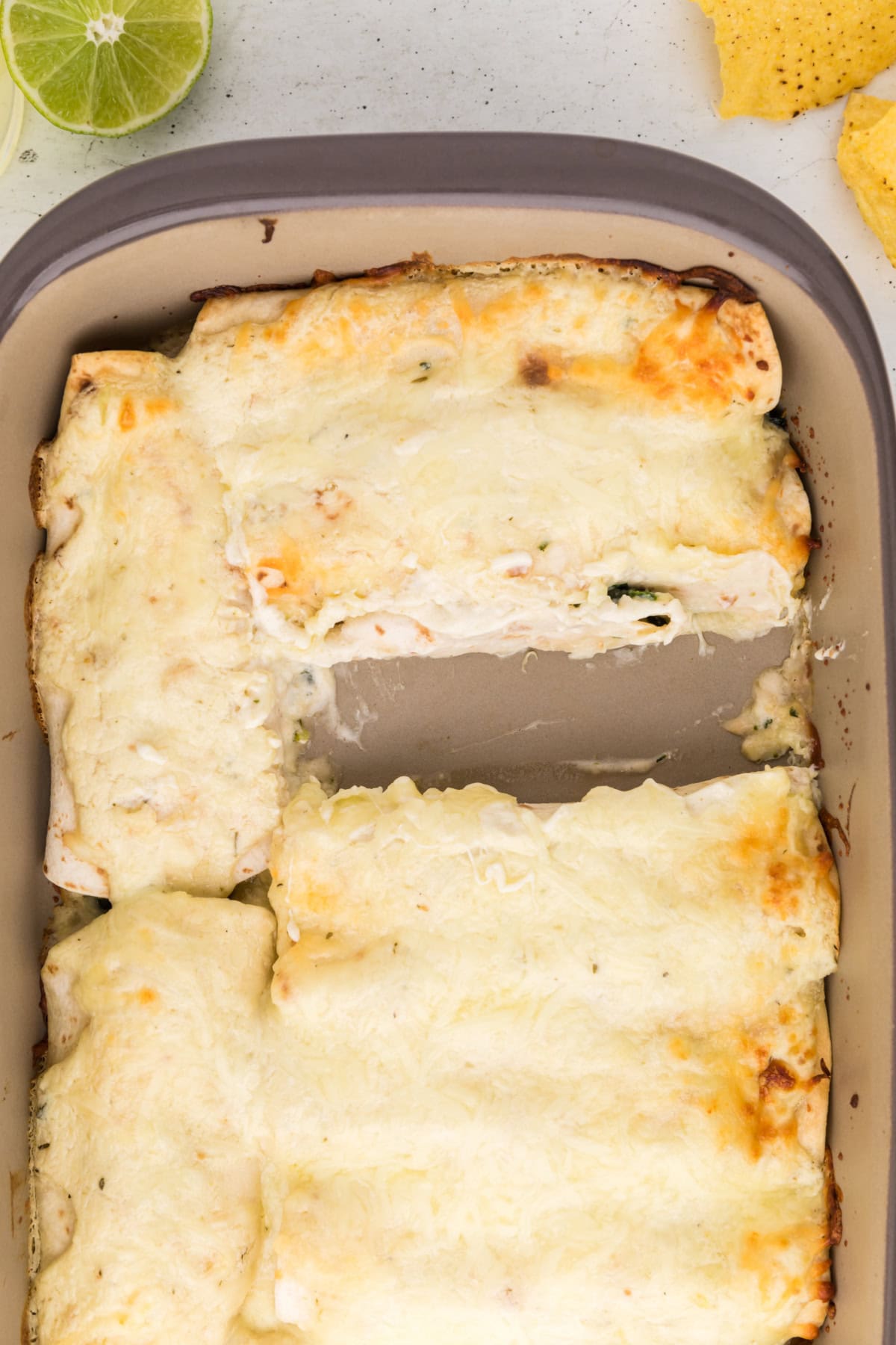 pan of creamy chicken spinach and mushroom enchiladas with one taken out
