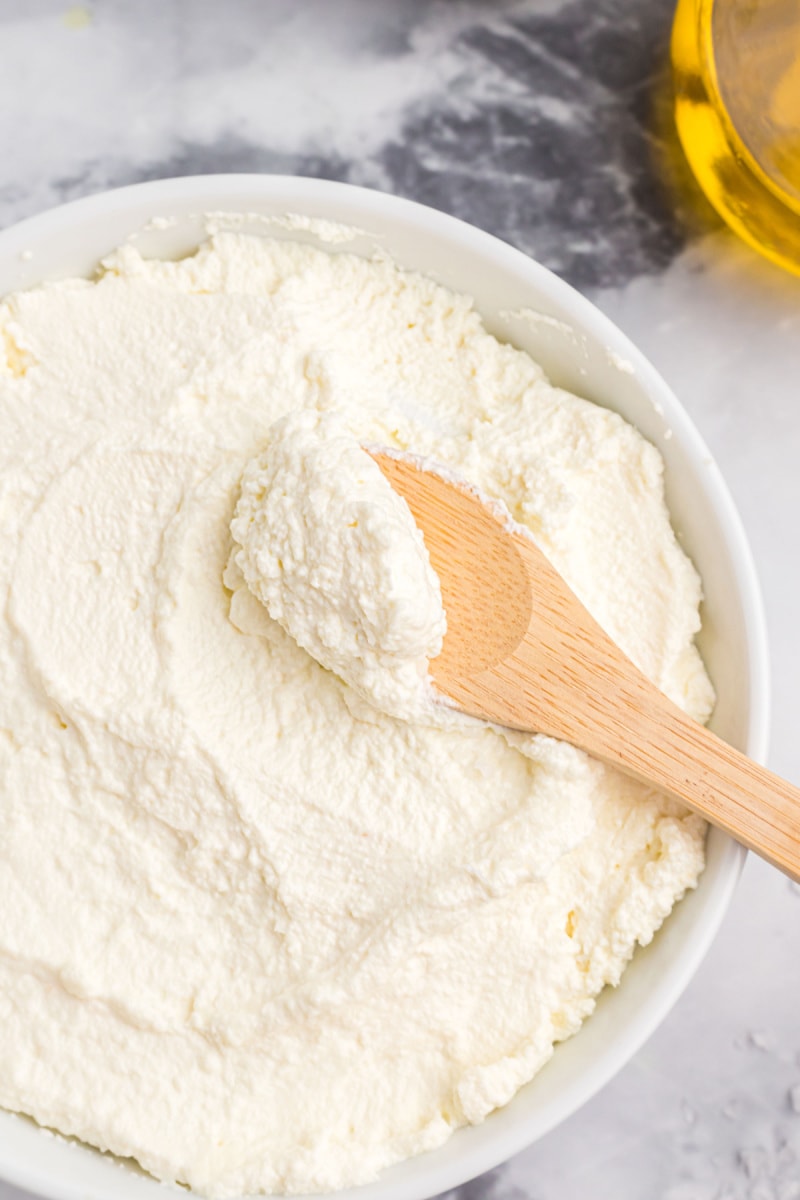 bowl of homemade ricotta cheese with wooden spoon