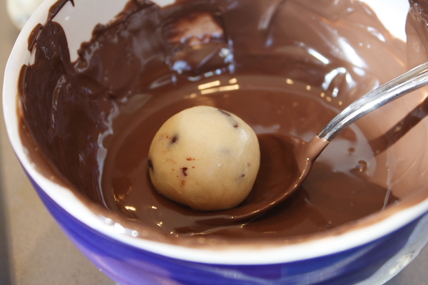 Chocolate Chip Cookie Dough dipping in melted chocolate in a blue bowl to make Truffles
