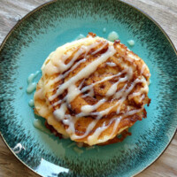 overhead shot of cinnamon roll pancakes with cream cheese drizzle on a teal green plate on a wooden board
