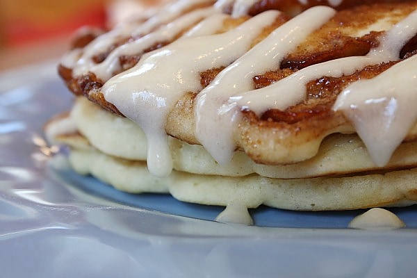 close up of cinnamon roll pancakes drizzled with cream cheese frosting on a blue plate