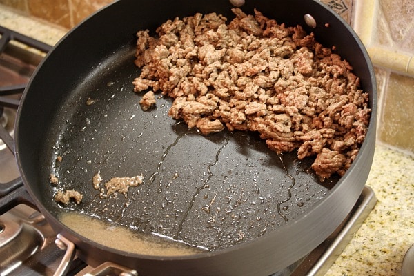 cooked ground beef in a skillet tipped to show collected oil in the pan