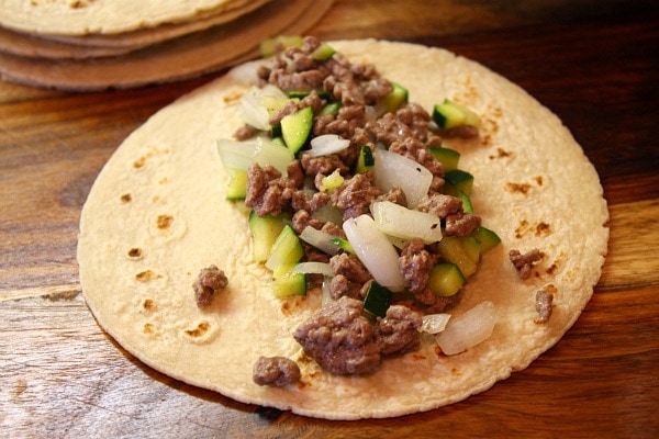 assembling beef enchiladas with filling on top of a flour tortilla