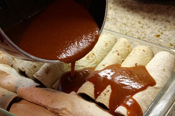 pouring enchilada sauce onto assembled beef enchiladas in a casserole dish