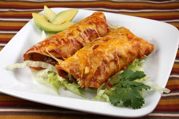 Two beef and cheese enchiladas on a plate with lettuce and avocado slices