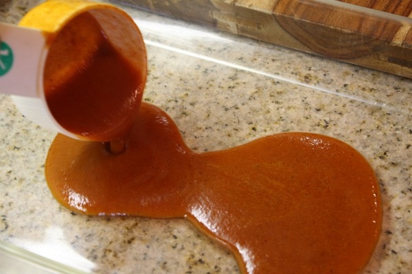 pouring enchilada sauce into a pyrex casserole dish