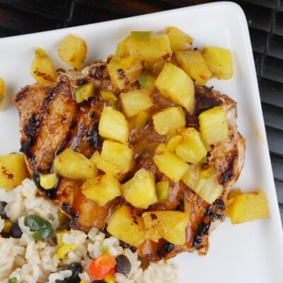 overhead shot of chili rubbed pork chops with pineapple and rice on a white plate