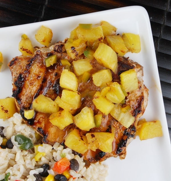 overhead shot of chili rubbed pork chops with pineapple and rice on a white plate