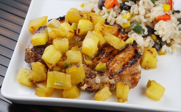 close up of chili rubbed pork chop on a white plate topped with pineapple