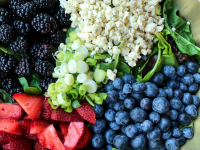 overhead shot of ingredients for triple berry salad set in a green bowl on a wooden surface