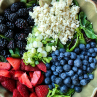 overhead shot of ingredients for triple berry salad set in a green bowl on a wooden surface