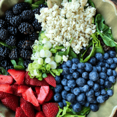 overhead shot of ingredients for triple berry salad set in a green bowl on a wooden surface