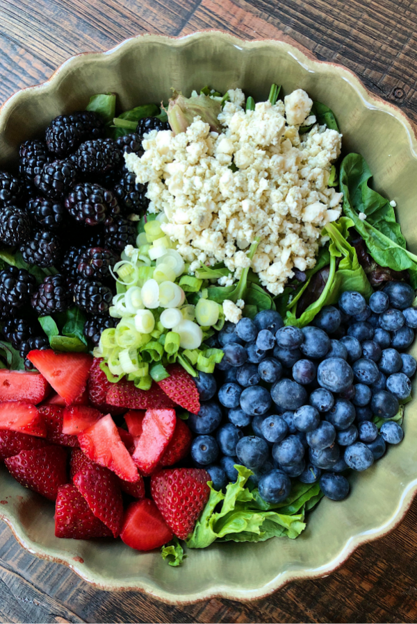 overhead shot of ingredients for Triple Berry Salad with Gorgonzola Cheese set in a green salad bowl on a wooden surface