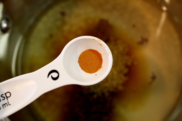 adding turmeric to a pan with a measuring spoon