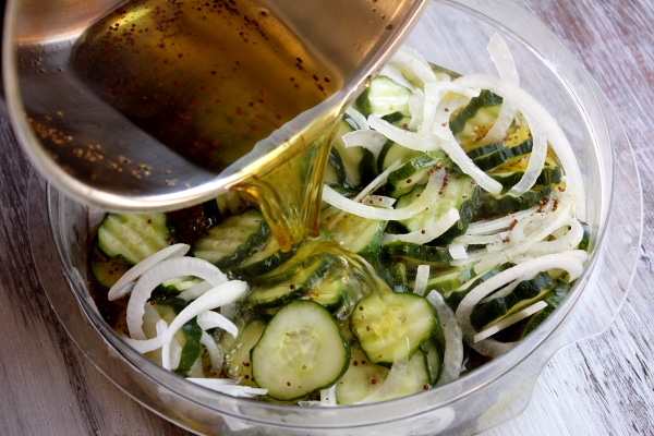 pouring pickling mixture into a glass bowl of bread and butter pickles