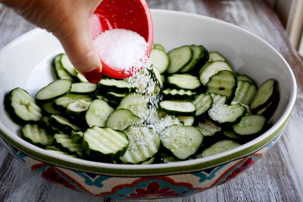 adding salt to a white bowl of sliced cucumbers