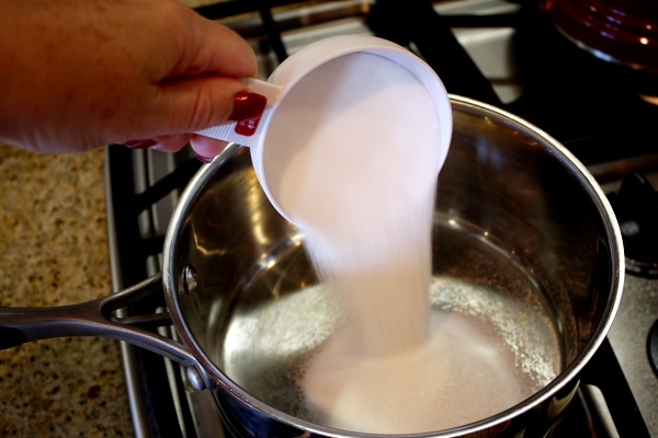 adding sugar to a pan with a measuring cup