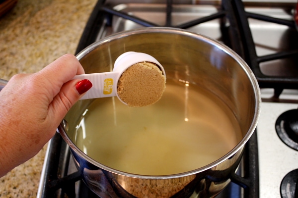adding brown sugar to a pan with a measuring cup