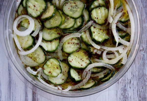overhead shot of bread and butter pickles marinating in a glass bowl