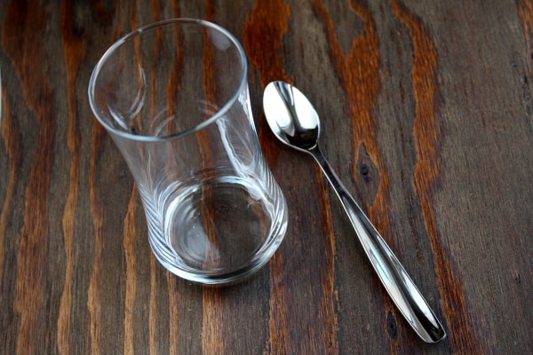 tall, empty glass sitting on a wooden board with a spoon alongside
