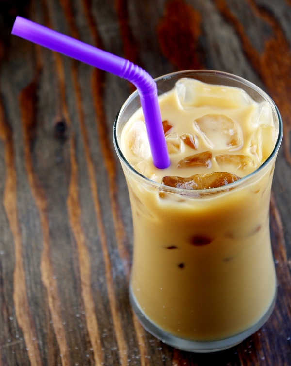 glass of iced coffee with a purple straw sitting on a wooden board