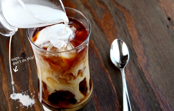 pouring cream into iced coffee and cream spilling on the board with spoon sitting on the side