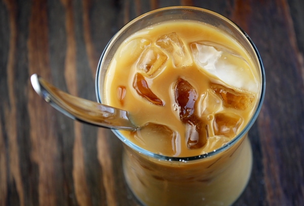 overhead shot of iced coffee with a spoon in it sitting on a wooden board