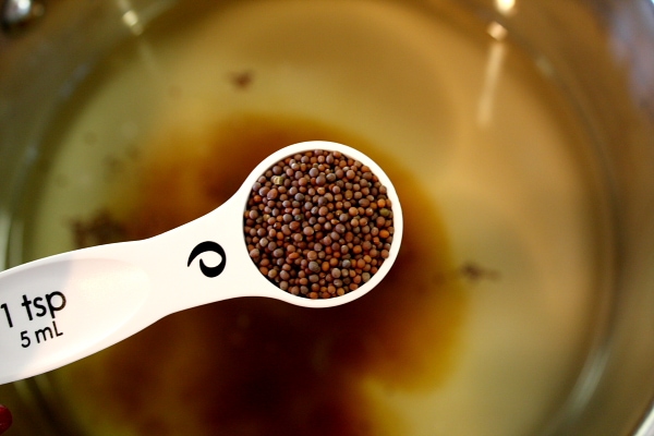 adding mustard seeds to a pan with a measuring spoon