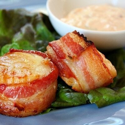 two bacon wrapped scallops on a blue plate garnished with lettuce leaf and served with sauce