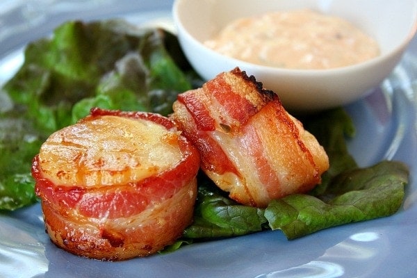 two bacon wrapped scallops on a blue plate garnished with lettuce leaf and served with sauce