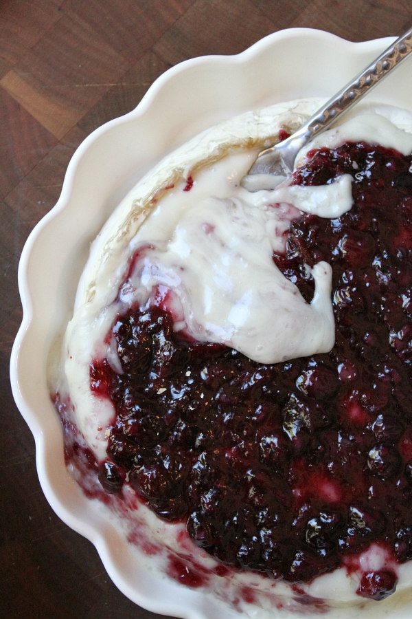 overhead shot of baked brie with blueberry sauce in a scalloped white pie dish